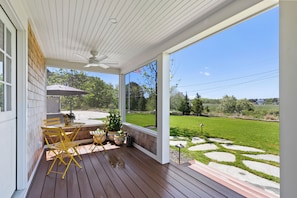 A covered porch with a table and chairs, a ceiling fan, and a view of a grassy yard.