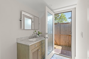 A bathroom with a marble sink, wooden cabinets, a glass shower door, and a view of a wooden deck.