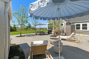 An outdoor patio area with a covered seating area, a fire pit, and a lawn.