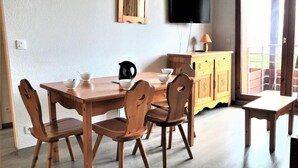 Een eetruimte met een houten tafel en stoelen, een aan de muur bevestigde televisie en een schuifdeur naar een buitenruimte.