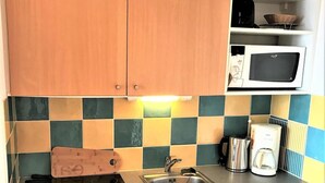 Een kleine keuken met houten kastjes, een roestvrijstalen spoelbak, een magnetron en een koffiezetapparaat.