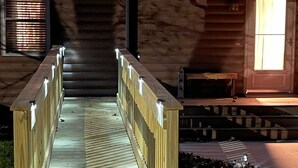 A wooden bridge leading to a building with a sloped roof and a window with blinds.