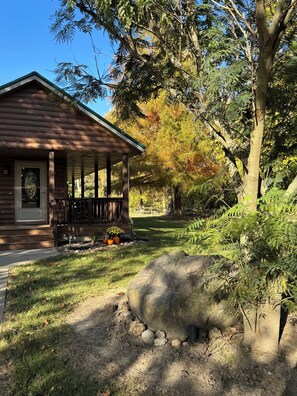 A rustic cabin with a porch, surrounded by a well-maintained lawn and trees.