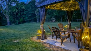 A gazebo with string lights, wooden chairs, and a table in a backyard.