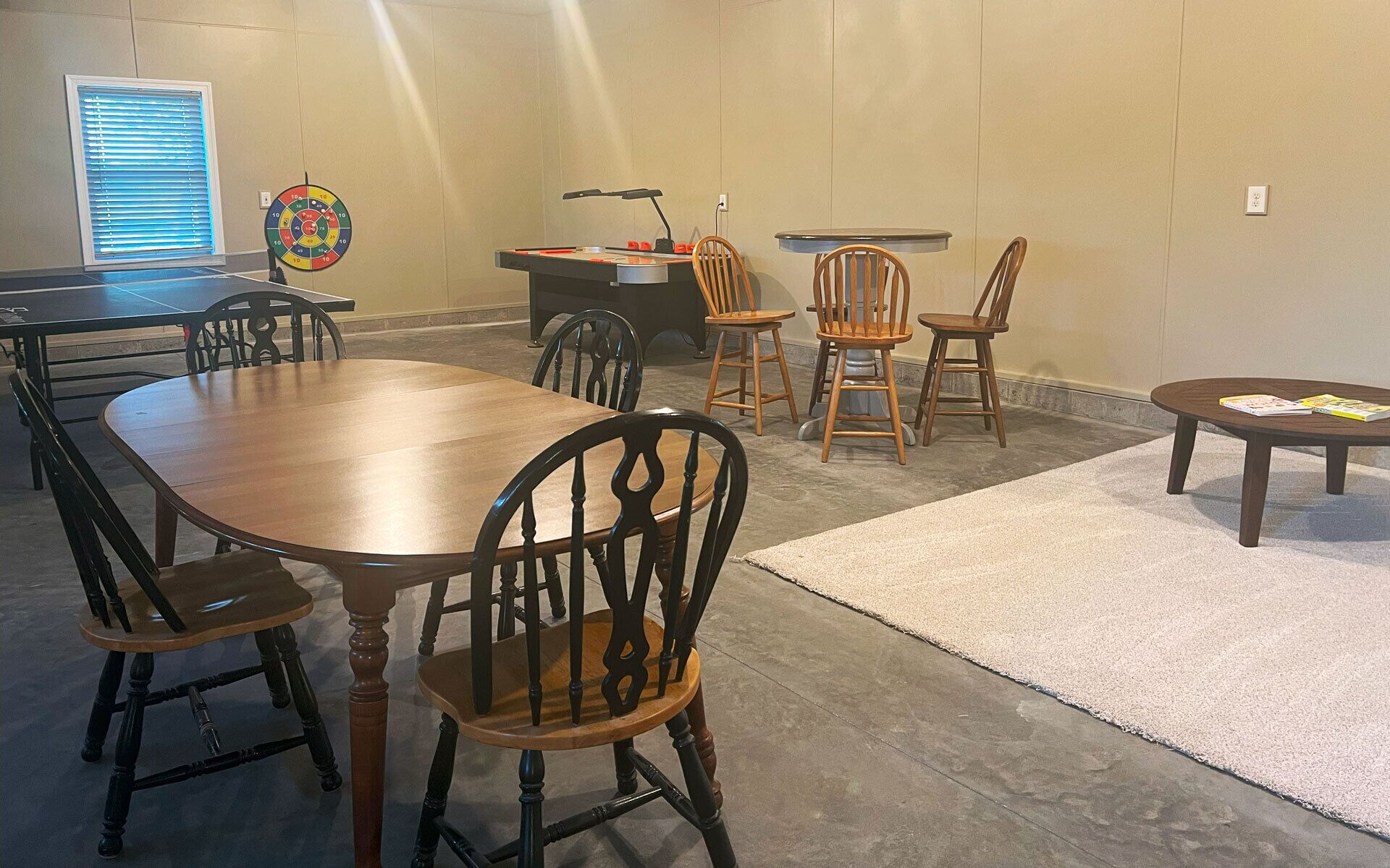 A conference room with a long table, several chairs, a small desk with a lamp, and a dartboard on the wall.
