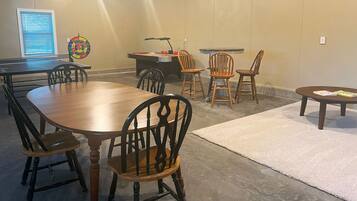 A conference room with a long table, several chairs, a small desk with a lamp, and a dartboard on the wall.