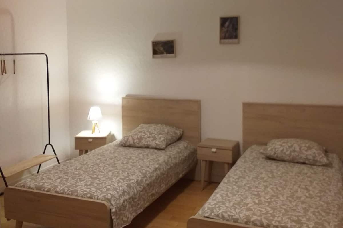 Quarto com duas camas de madeira, uma mesa de cabeceira com luminária e um guarda-roupa.