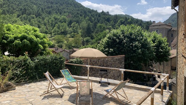 A terrace with stone flooring, two lounge chairs, a table, and an umbrella. - GITE AVEC TERRASSE  (Peyreleau)