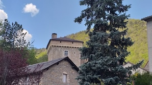 A stone building with a pitched roof, surrounded by lush greenery and a tall coniferous tree. - GITE AVEC TERRASSE  (Peyreleau)