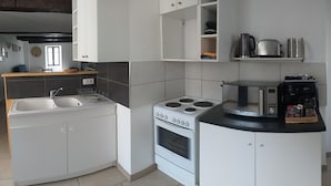 A modern kitchen with white cabinets, a stove, a microwave, and a coffee maker. - GITE AVEC TERRASSE  (Peyreleau)