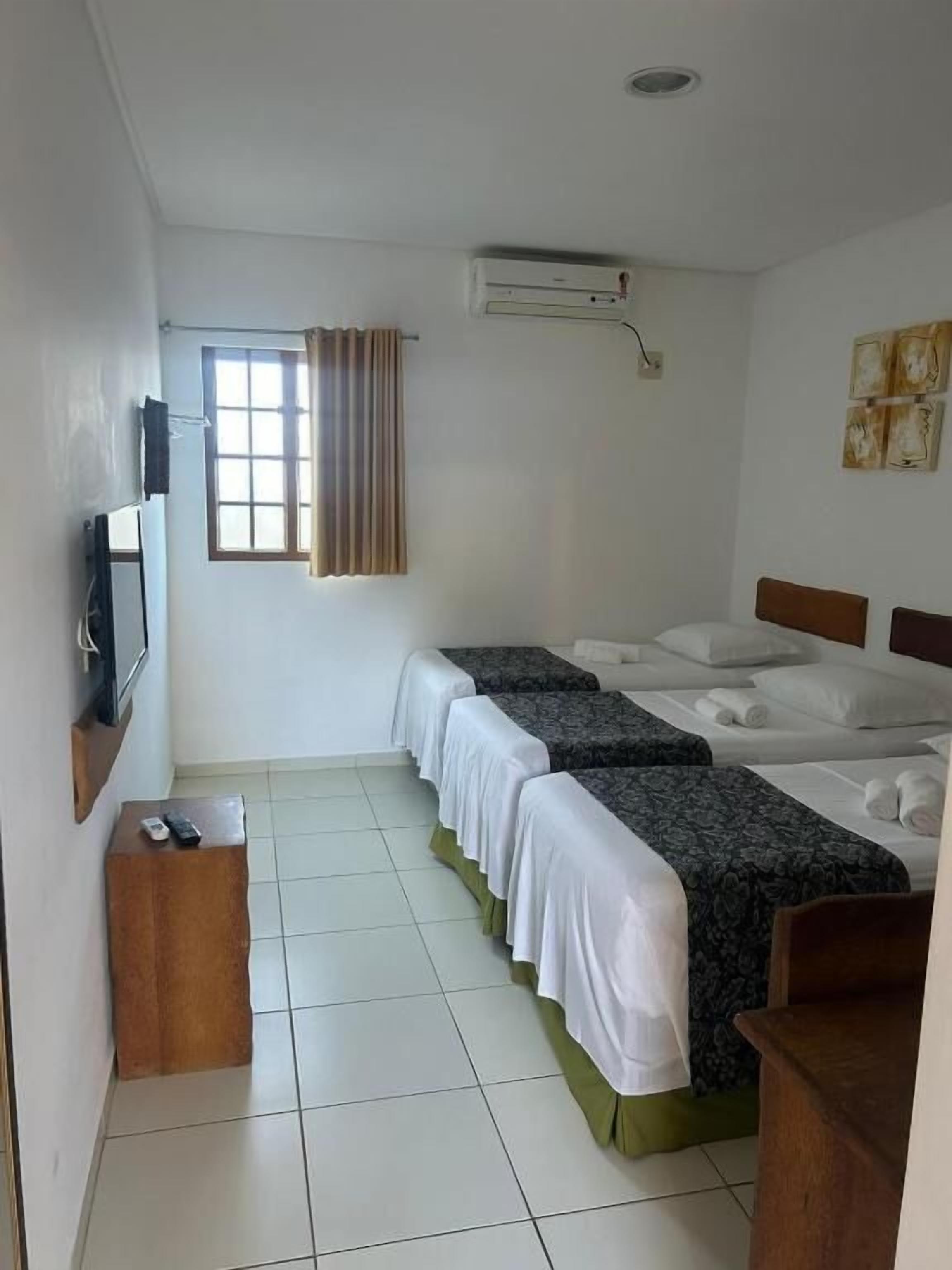 A hotel room with two beds, a TV, a window with curtains, and a wall-mounted air conditioner.