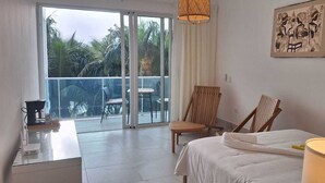 Een hotelkamer met een bed, een bureau, een stoel, een balkon met een tafel en stoelen, en een schilderij aan de muur.