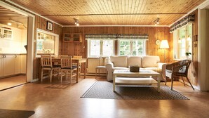 Una stanza accogliente con pareti e soffitto in legno, una zona pranzo con sedie e tavolo, un divano e una lampada.