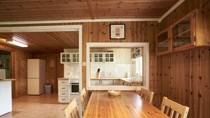 Una cucina con pannelli in legno, un tavolo e sedie di legno, mobili bianchi e un frigorifero.