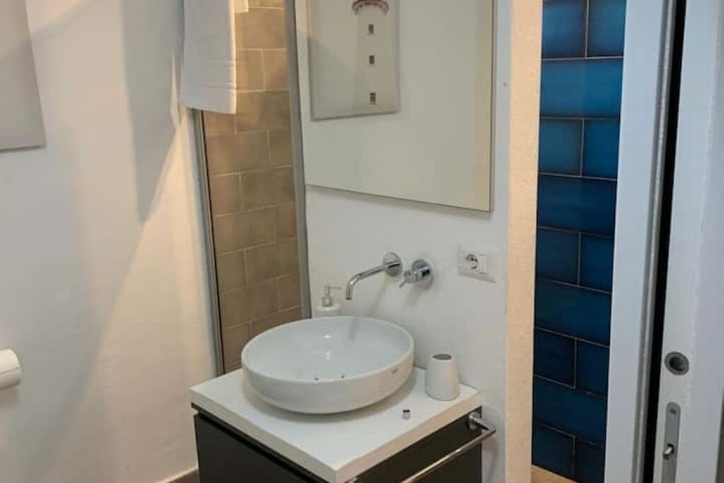 Een badkamer met een wit wastafel, een spiegel erboven en een blauwe betegelde muur.