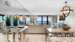 A spacious living area with a large sofa, dining table, and chairs. There is a view of the ocean through large windows. - 🚢Beachfront Complex-Private Beach-Incredible Gulf Views-Edgewater #1007🚢 (Miramar Beach)