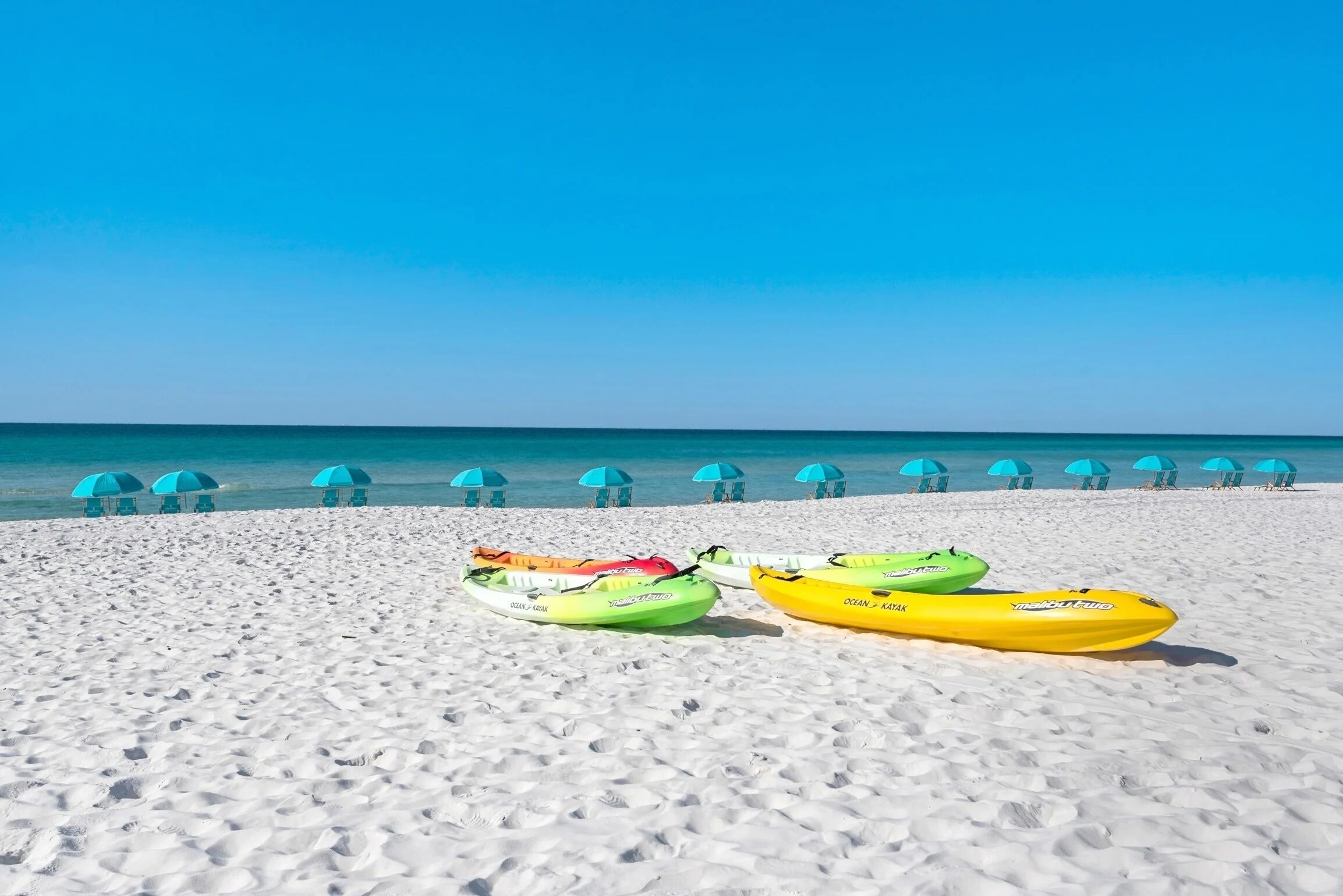 A beach with kayaks and umbrellas.