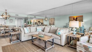 A spacious living room with a sectional sofa, a coffee table, and a dining area with a chandelier. - 🚢Beachfront Complex-Private Beach-Incredible Gulf Views-Edgewater #1007🚢 (Miramar Beach)