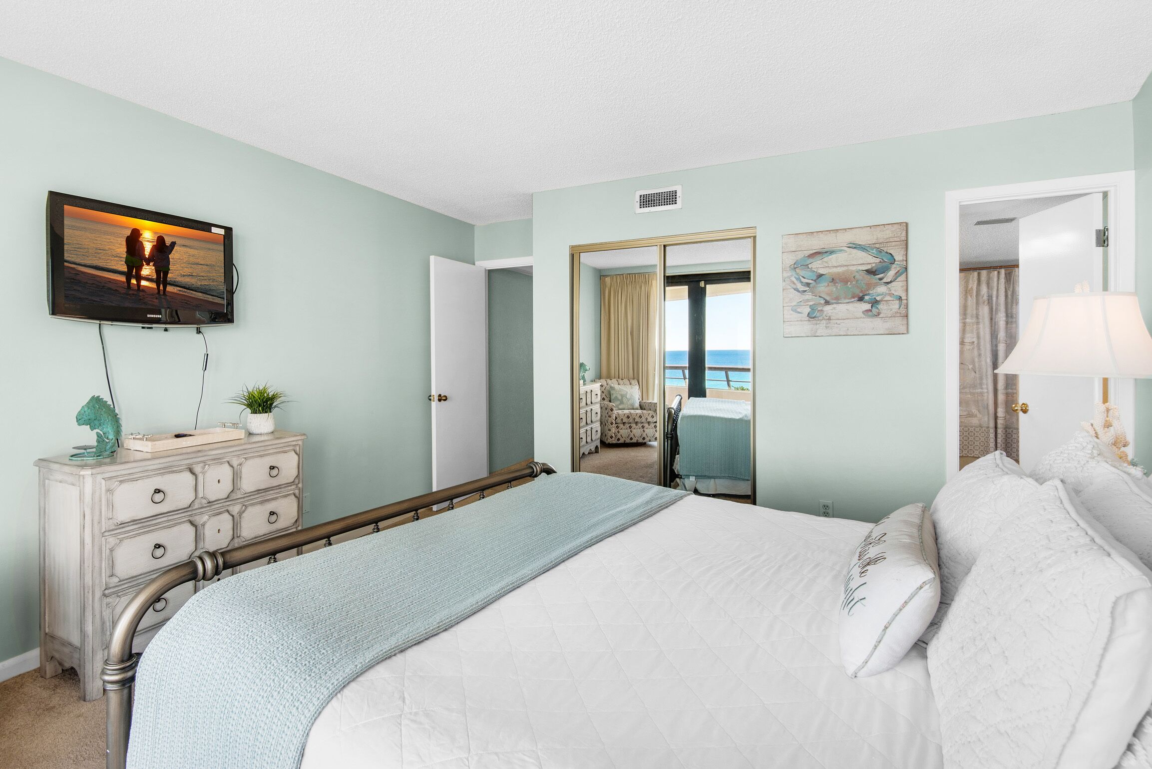 A bedroom with a bed, a dresser, a television, and a view of the ocean through an open door.