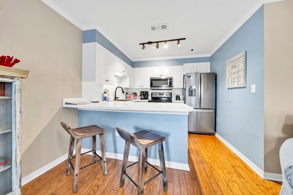 A modern kitchen with white cabinets, a stainless steel refrigerator, and a central island with stools.