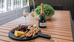 A wooden table with a bottle of champagne, two glasses, a cheese board with grapes and crackers, and a potted plant. - Central Haven Milton 4BR Sleeps 10 (Milton)