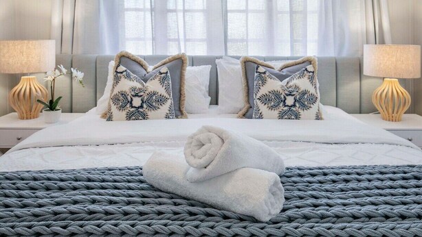 A neatly made bed with a rolled white towel, two patterned pillows, and a grey knitted throw. - Central Haven Milton 4BR Sleeps 10 (Milton)