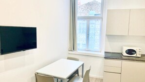 Habitació petita i lluminosa amb taula i cadires blanques, televisió de pantalla plana, finestra amb vista a edificis i microones a la barra.
