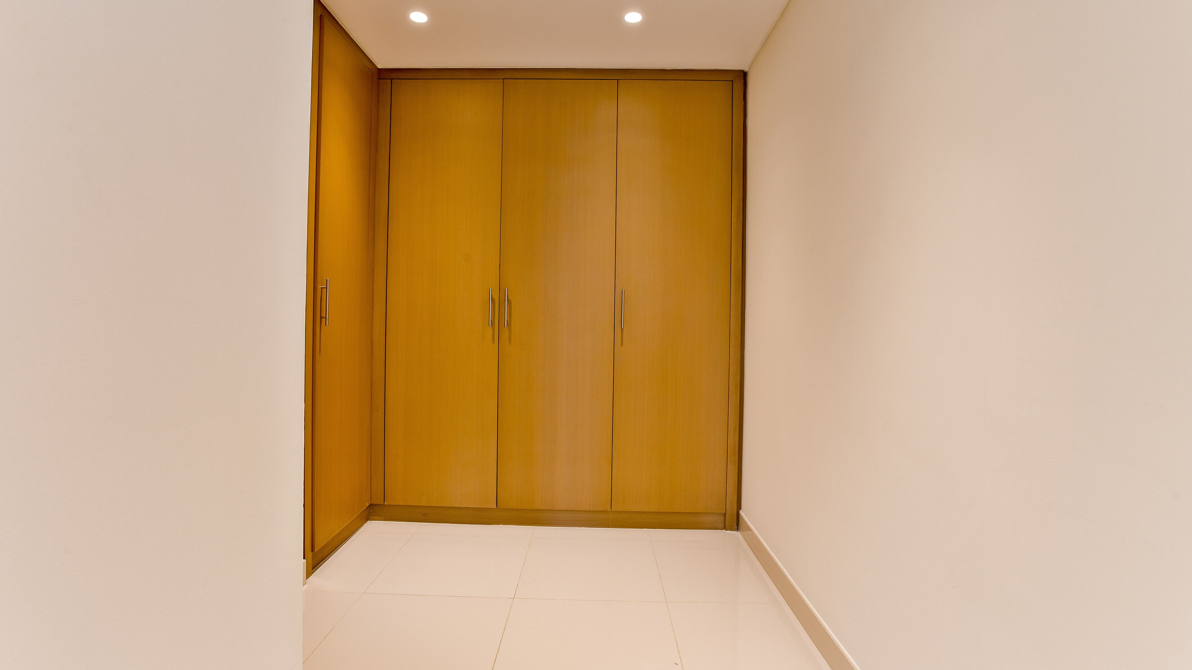Una habitación con un amplio armario de madera, suelo de baldosas blancas e iluminación empotrada.