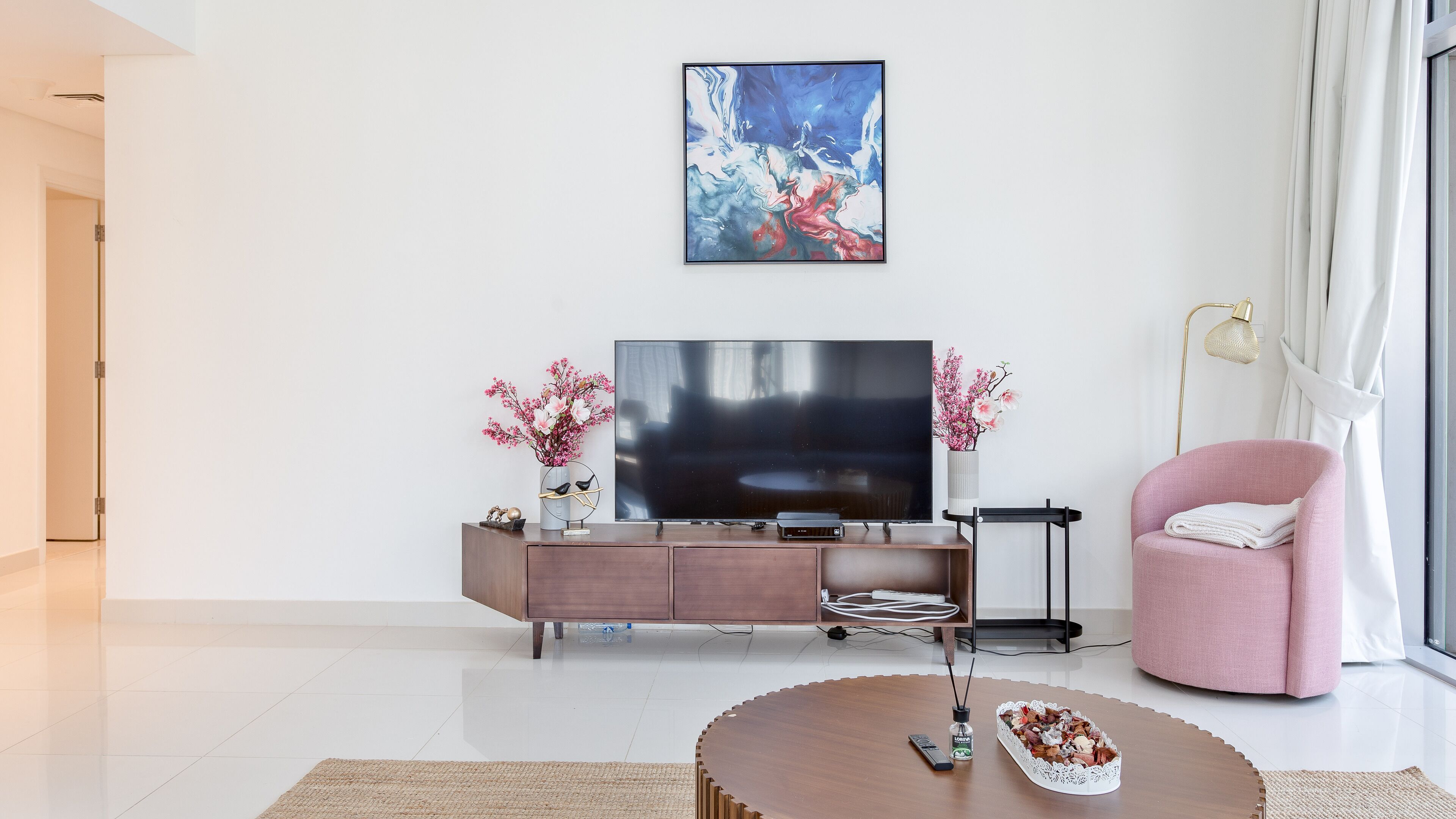 Un salon moderne avec un téléviseur à écran plat, un fauteuil rose et une table basse.