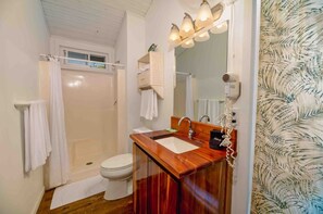 Ein Badezimmer mit einem Holzkosmetikschrank, einer weißen Toilette, einer Dusche mit weißem Duschvorhang und einem beleuchteten Spiegel.