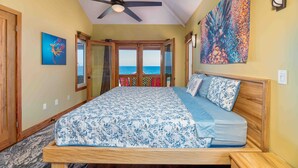 Een slaapkamer met een bed, een plafondventilator, uitzicht op zee en kunstwerken aan de muren.