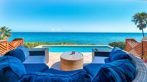 Een terras aan het zwembad met uitzicht op de oceaan, een klein rond tafeltje en blauwe, beklede zitplaatsen.