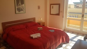 A hotel room with a large bed, a nightstand, a bedside lamp, a framed picture of the Eiffel Tower, a mirror, and a balcony with a view of buildings. - Bilocale Ariosto Vista Mare Laterale (Gallipoli)
