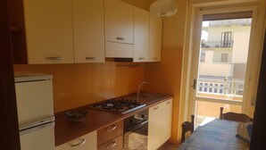 A kitchen with white cabinets, a gas stove, and a sink. There is a dining table with a map and a chair. - Bilocale Ariosto Vista Mare Laterale (Gallipoli)