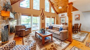 A spacious living room with a fireplace, large windows, and a high ceiling.