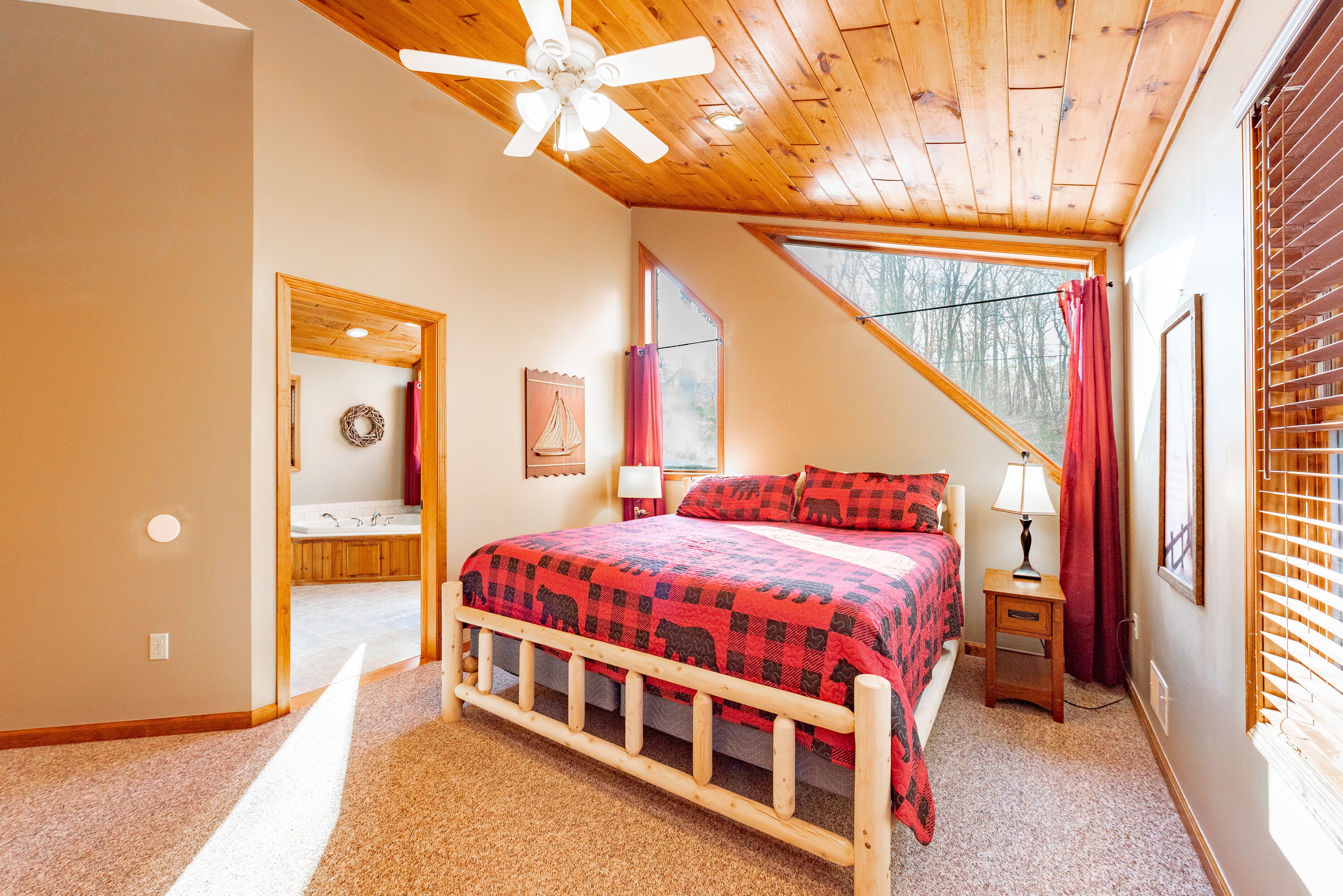 Ein Schlafzimmer mit Holzboden, einem Bett mit rot-schwarz karierter Bettdecke, einem Nachttisch mit Lampe und einem Fenster mit Vorhängen.