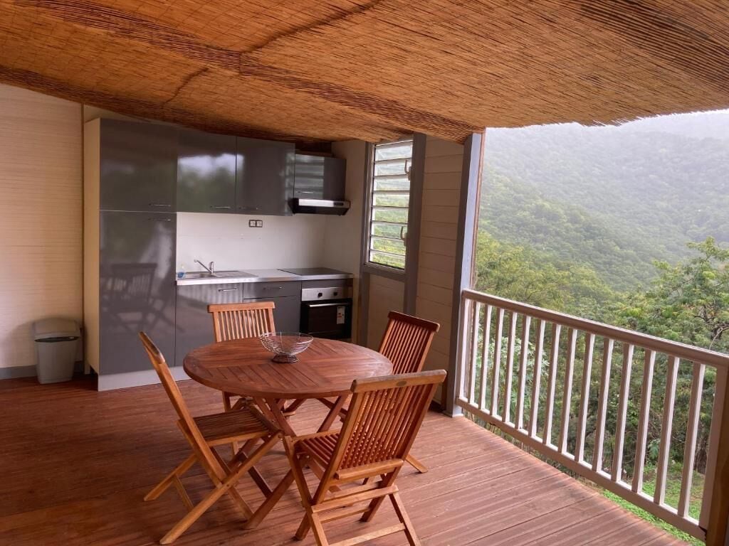 A wooden deck with a round table and chairs, a kitchen area with cabinets and a sink, and a view of a mountainous landscape.