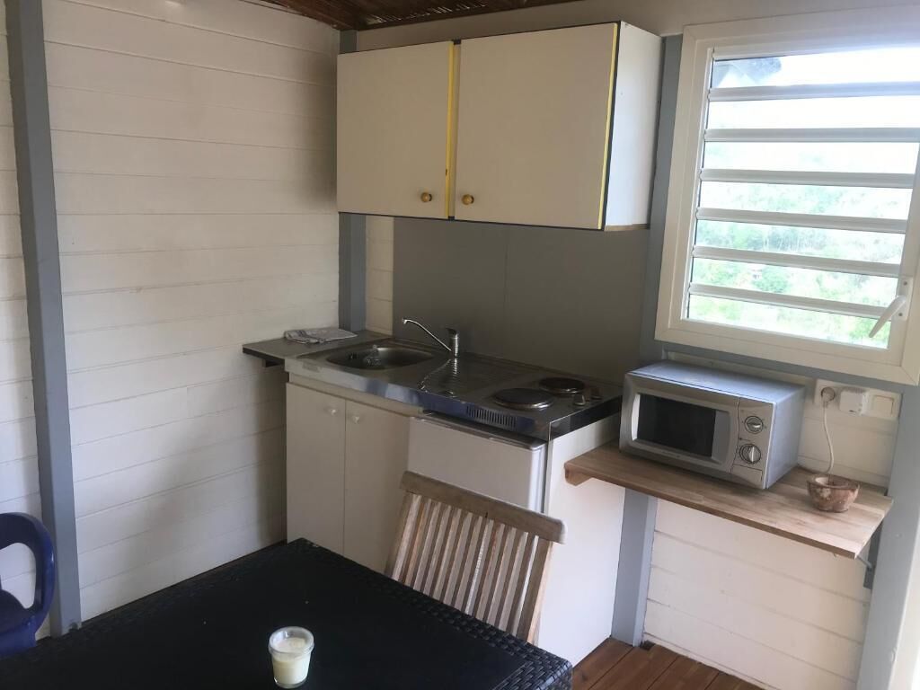 Eine kleine Küche mit weißen Schränken, einer Mikrowelle, einem Spülbecken und einem Fenster mit Jalousien.