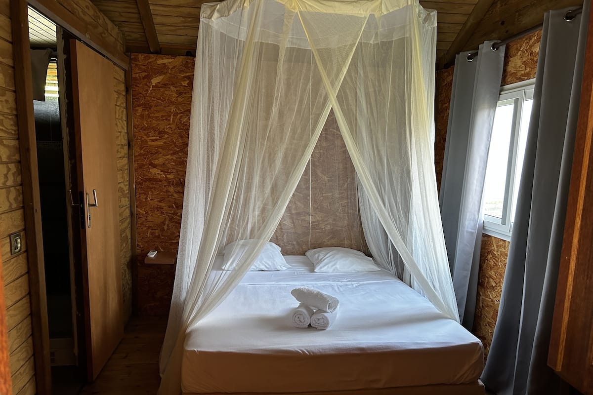 A room with a bed under a canopy, wooden walls, a door, and a window with curtains.