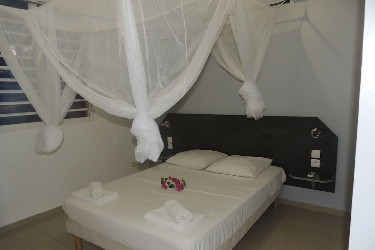 A bed with white linens, a bedside table with a remote control, and a decorative flower arrangement.
