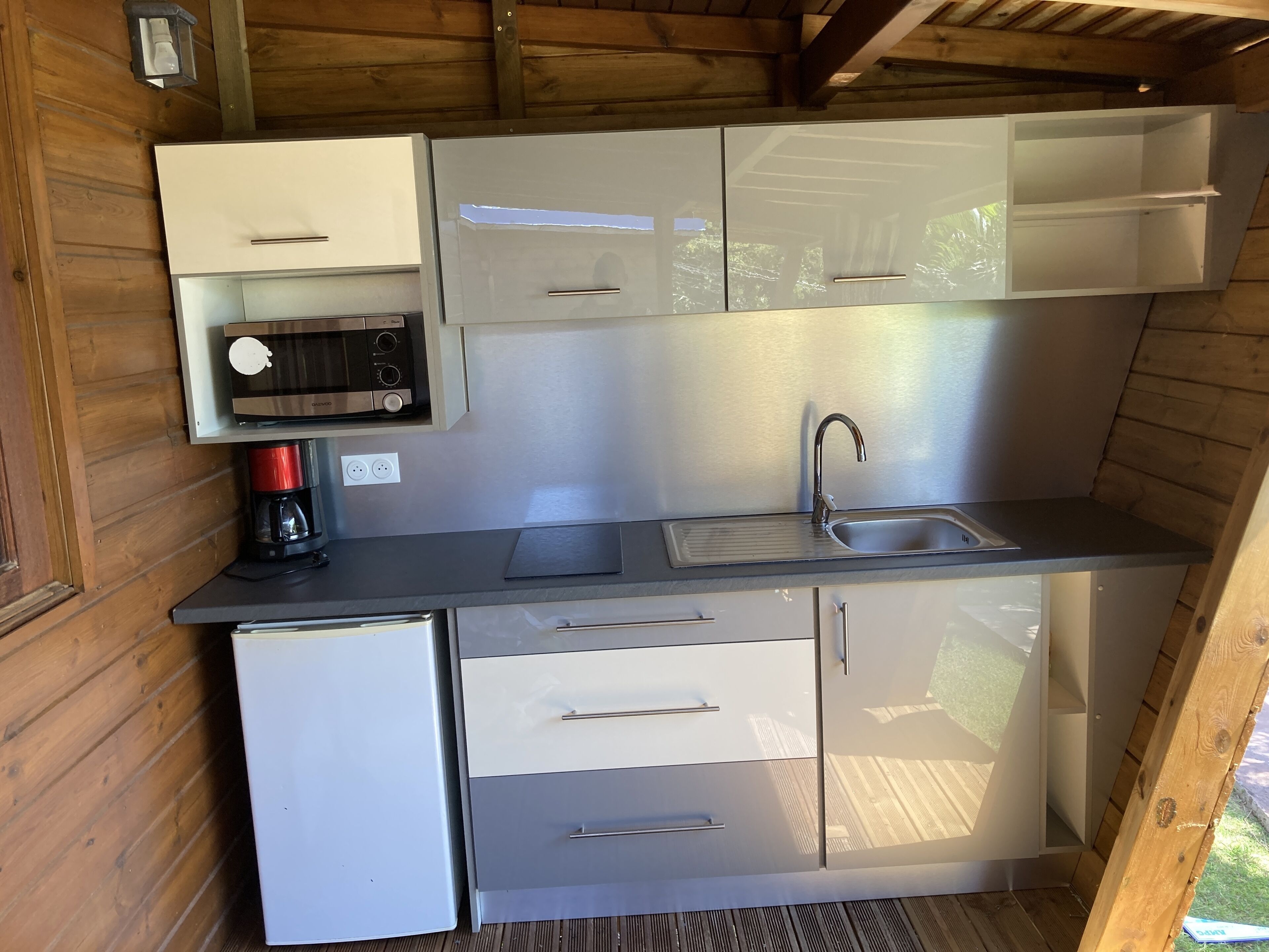 A compact kitchen with a microwave, coffee maker, sink, and cabinets.