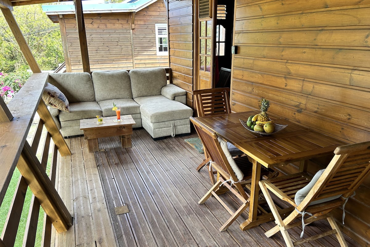 A wooden deck with a sofa and a table set up for dining, surrounded by wooden railings.