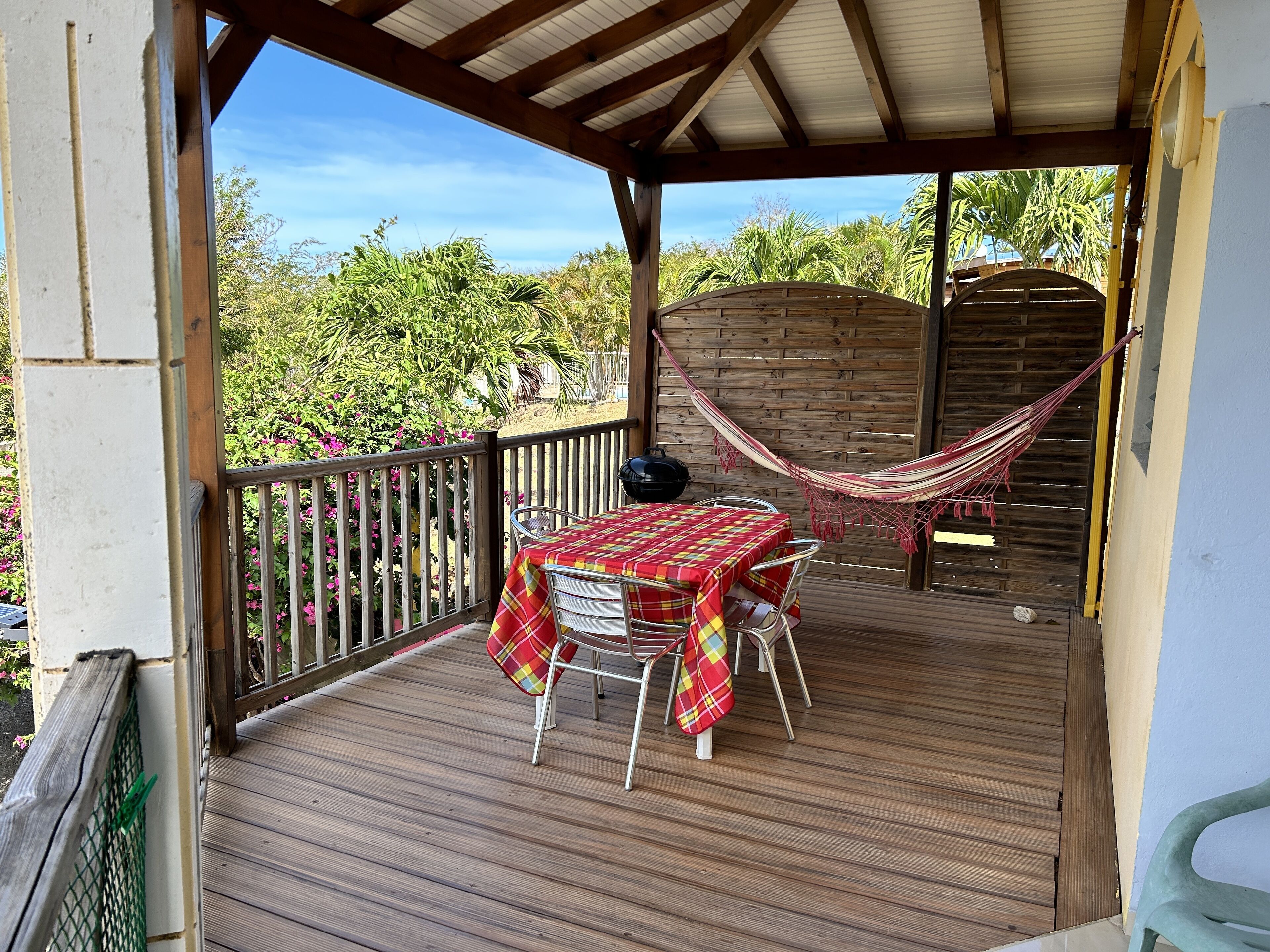 Un espace extérieur abrité, doté d’une terrasse en bois, d’une table recouverte d’une nappe à carreaux, de deux chaises et d’un hamac.