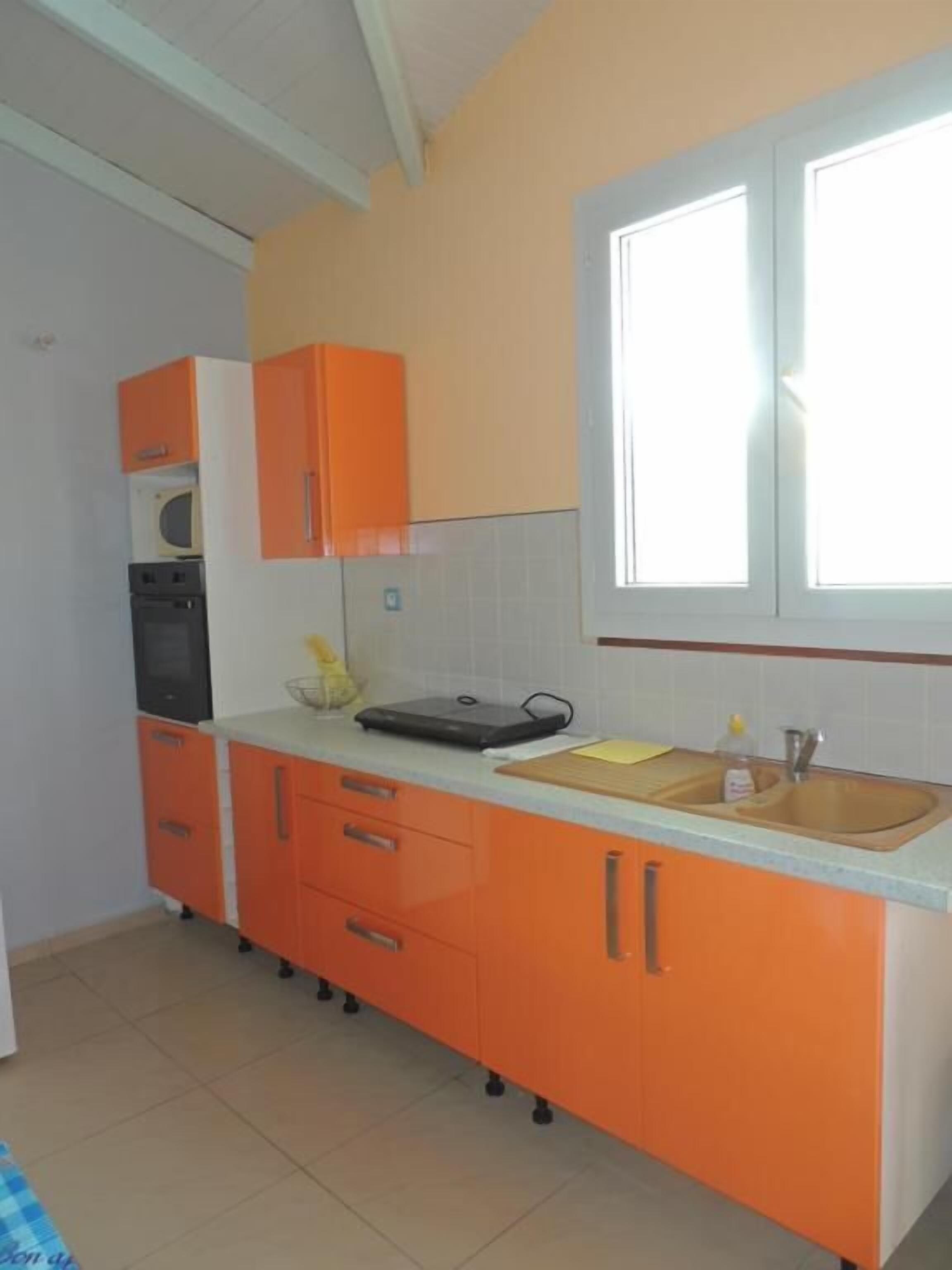 Een keuken met oranje kastjes, een magnetron, een broodrooster en een raam met jaloezieën.