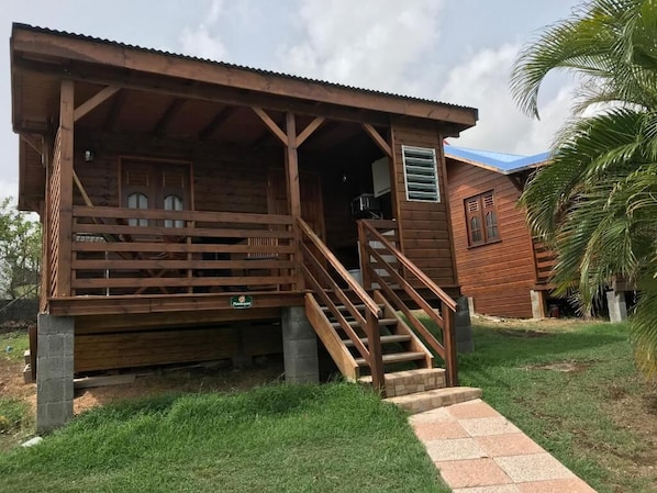 A wooden cabin with a porch and stairs leading to a door. - Hotel Gîtes Couleur Caraïbes (Bouillante)