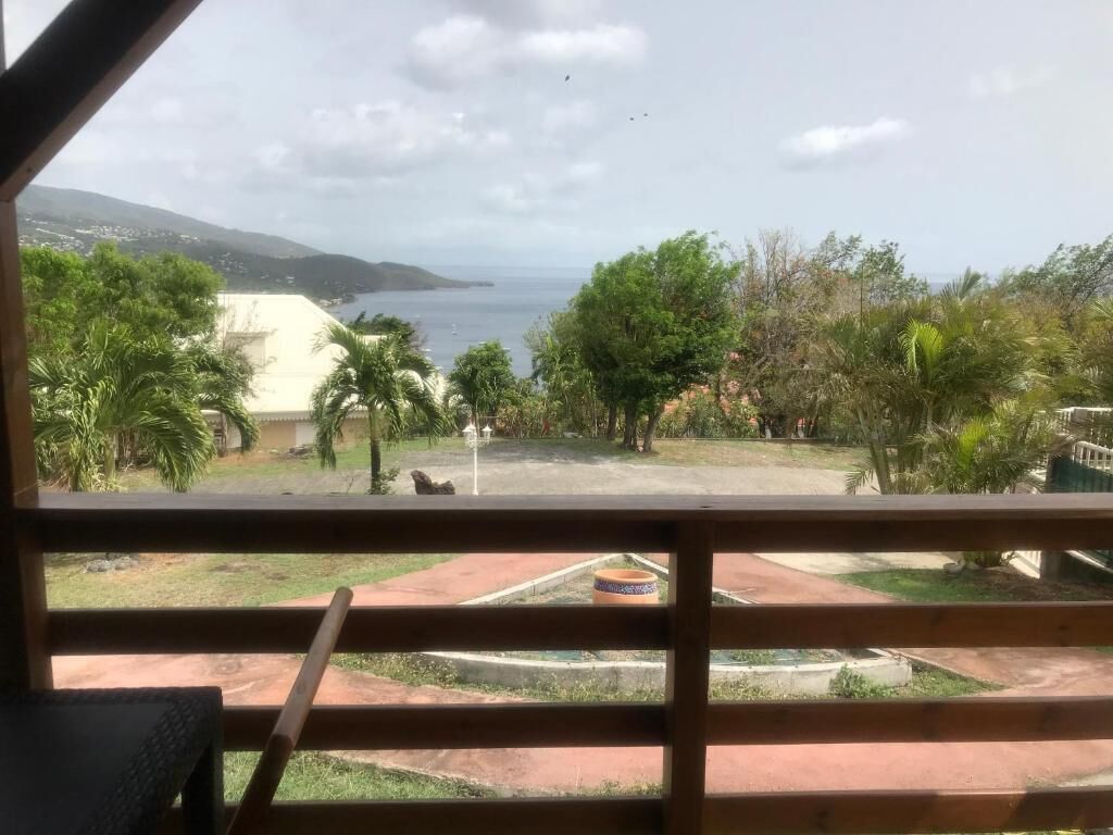 A view from a balcony with a wooden railing, overlooking a landscaped area with palm trees and a body of water.