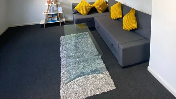 A modern living room with a gray sectional sofa, yellow cushions, a glass coffee table, and a ladder against the wall. - Apartment - Sleeps 4 & Excellent Transport Links (London)
