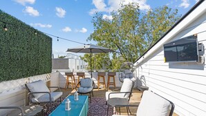 Una terraza en la azotea con mobiliario exterior, luces colgantes y vistas del horizonte urbano.