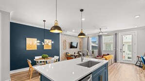 Una cocina moderna con una isla central, iluminación colgante y una zona de comedor con sillas y una mesa.