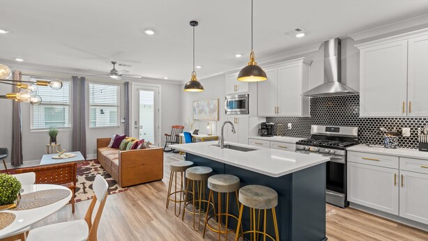 Una cocina moderna con gabinetes blancos, una campana extractora de acero inoxidable y una isla central con taburetes.